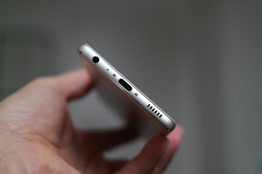 A close-up view of a person holding a smartphone, focusing on the charging port and headphone jack.