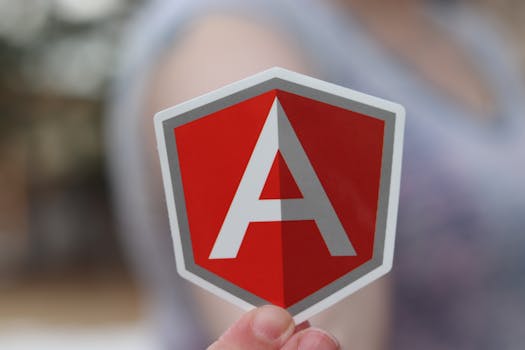 A person holding a red Angular logo sticker focusing on software development and security.