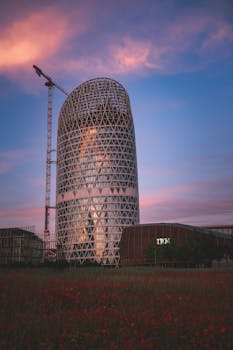 A contemporary skyscraper under construction with a crane against a vibrant sunset sky.